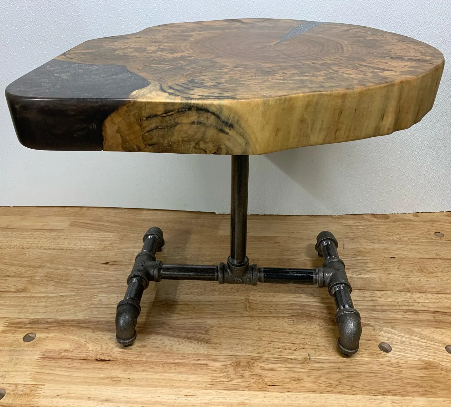 Asymmetric wood-and-dark-resin side table with a pipe-style metal base.