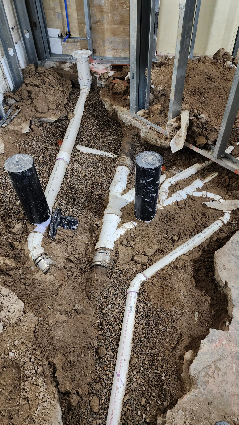 March 2023 progress photograph of the drain routing exposed below the basement slab.