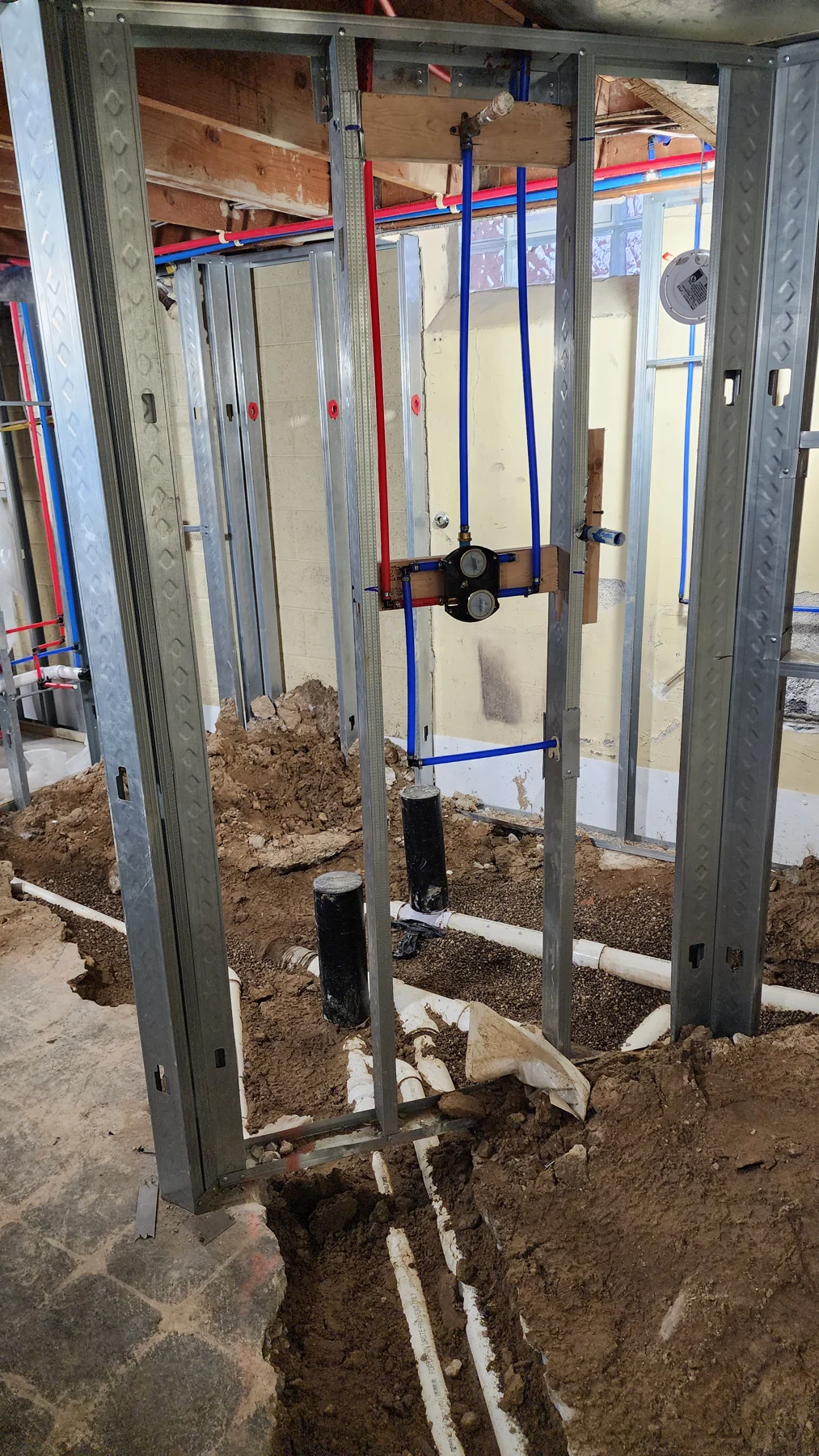 March 2023 progress photograph showing supply lines and a valve within the open metal-stud framing.