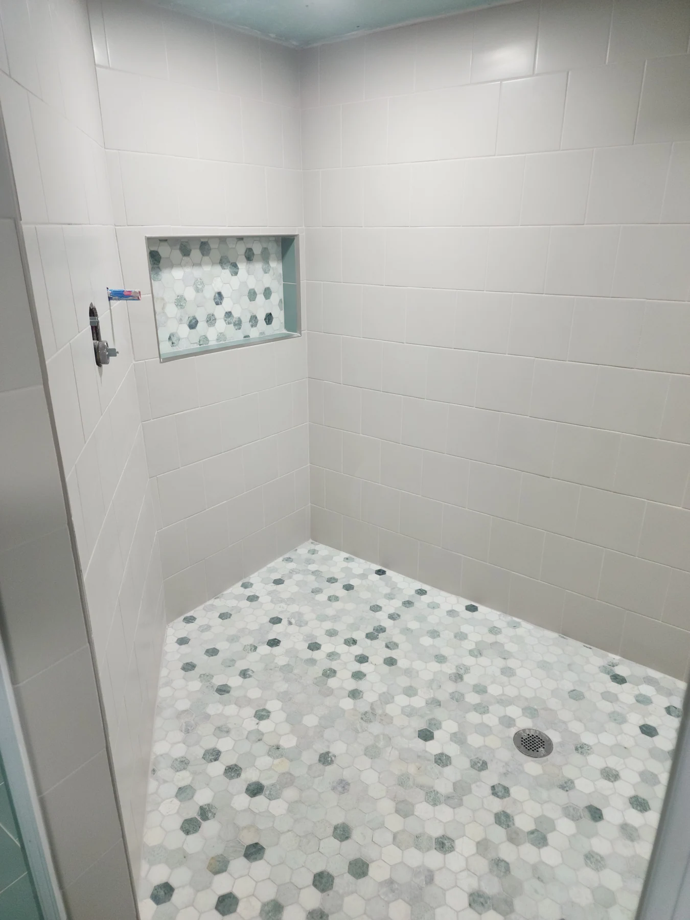 April 2023 shower tiling: light wall tile, a recessed niche, and a hexagonal-pattern floor.