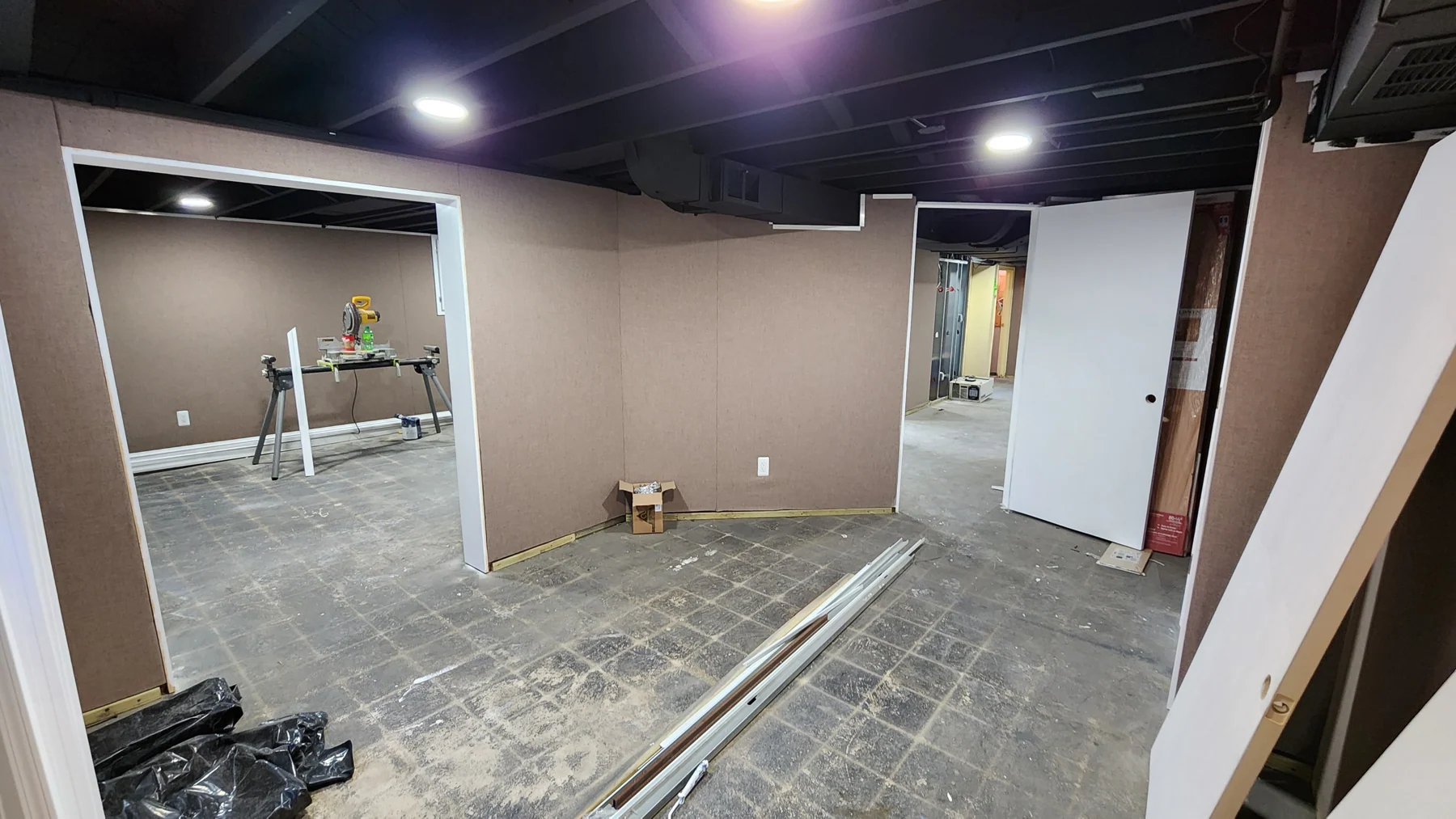 April 2023 basement progress, with boarded walls, door openings, and ceiling lighting.