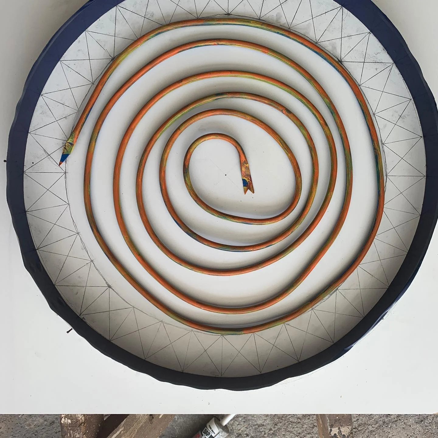 Copper spiral in a circular form over a geometric layout drawing.