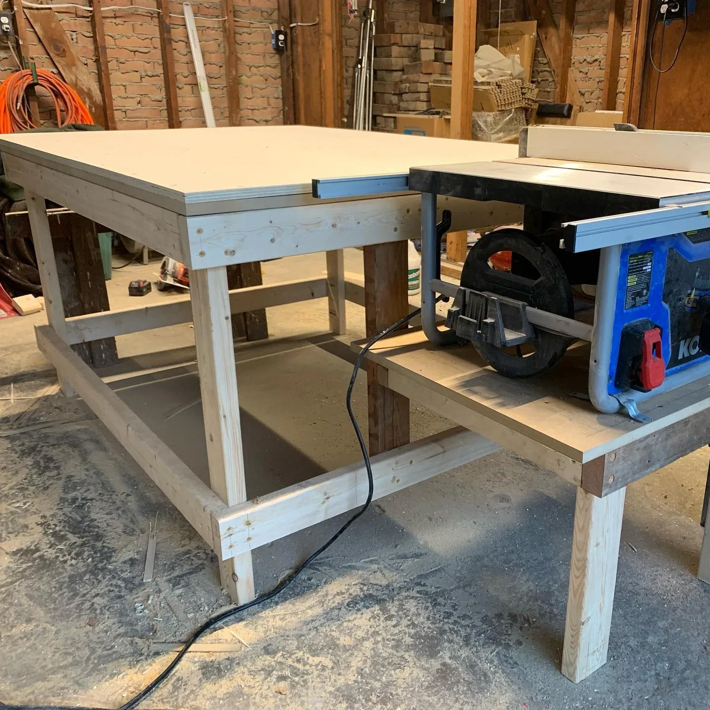The table-saw workbench with its broad laminated top, timber frame, and mounted vise.