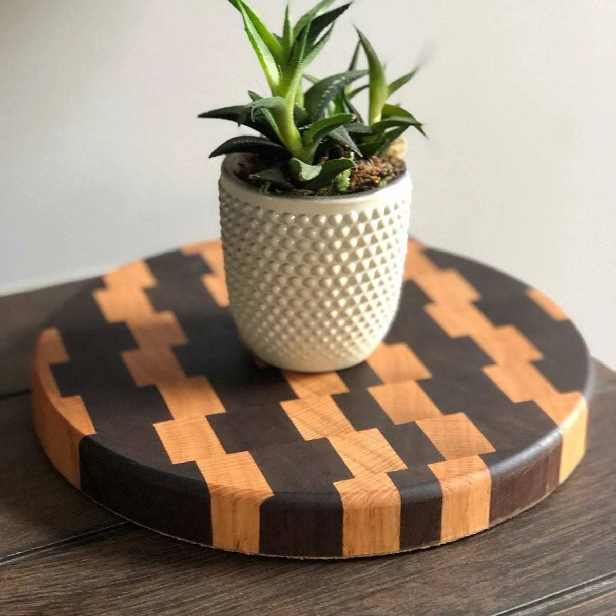 A patterned wooden trivet shown in use under a plant pot; customer photograph.
